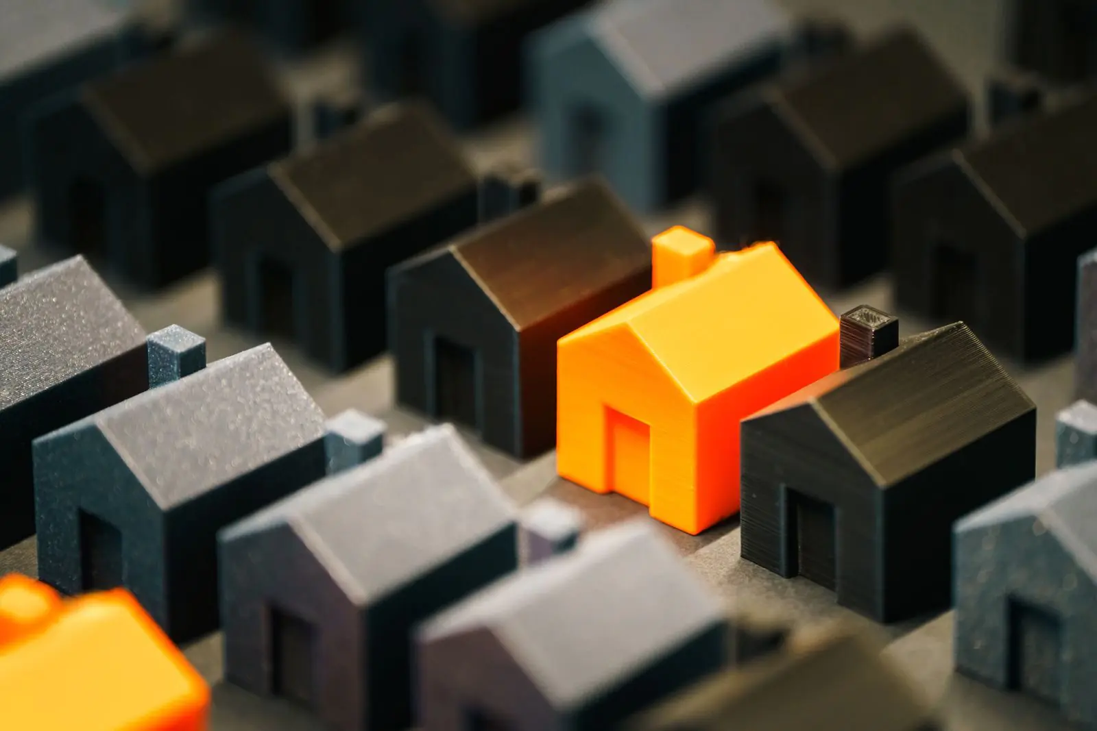 A standout orange house surrounded by smaller black and gray houses symbolizes uniqueness in a real estate context.
