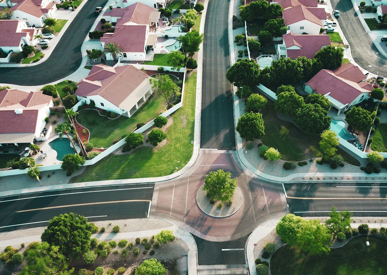 Aerial view of a suburban neighborhood featuring houses with red roofs, landscaped yards, and a circular intersection surrounded by greenery.